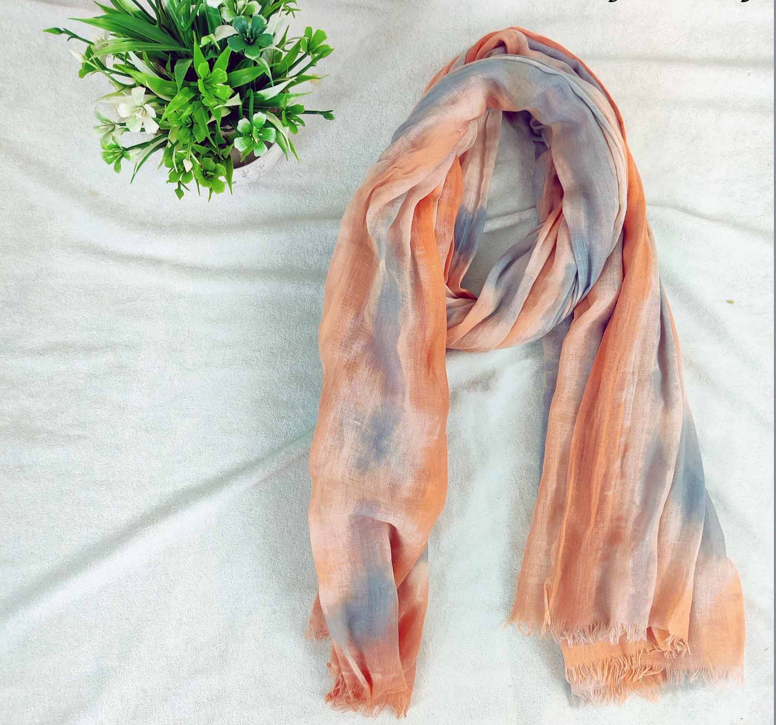 Peach and grey tie-dyed cotton scarf with frayed ends, draped on a white cloth