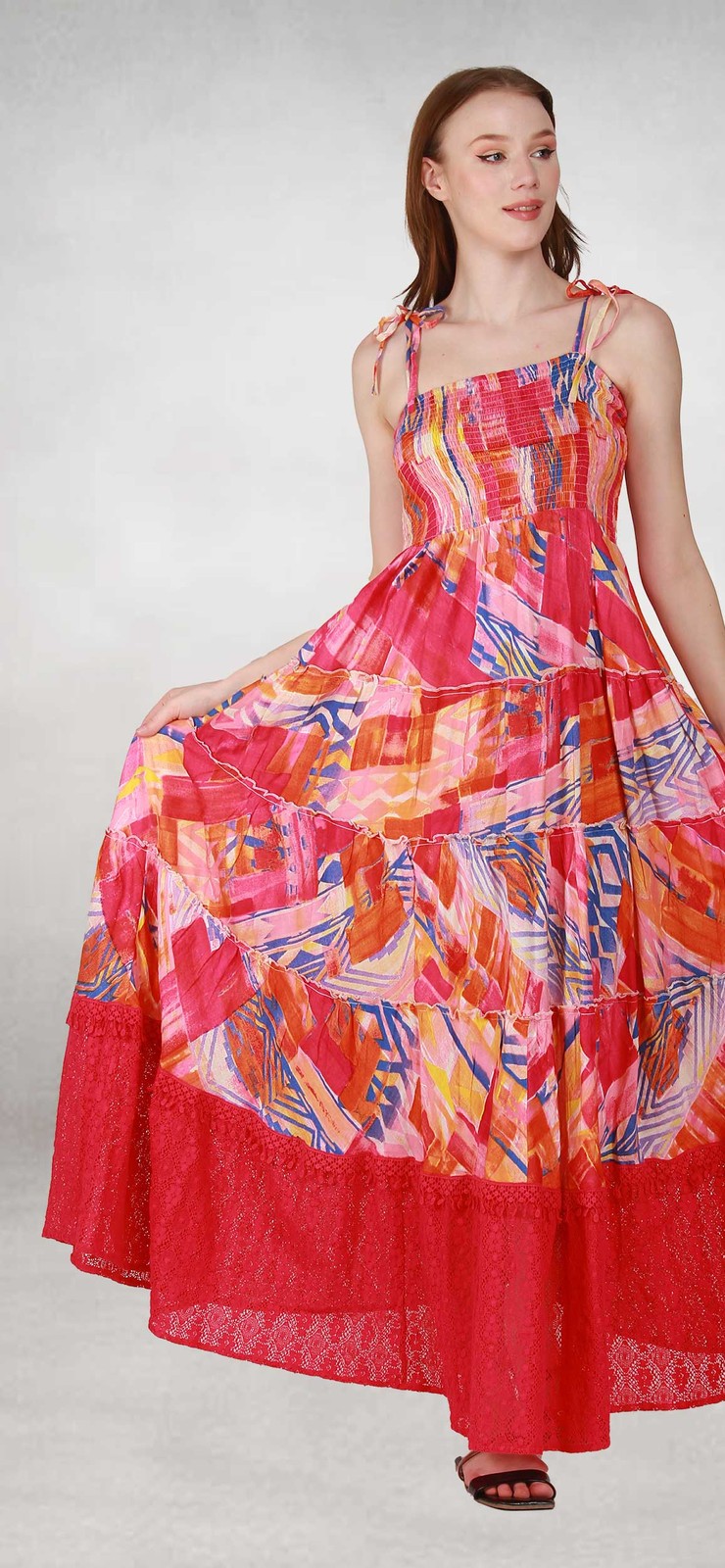 Woman in a pink and red geometric print viscose maxi dress with a smocked bodice, tie straps and a red net hem